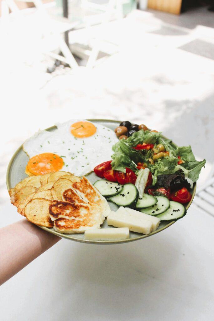 A fresh and balanced breakfast plate featuring fried eggs, salad, and sliced vegetables outdoors.